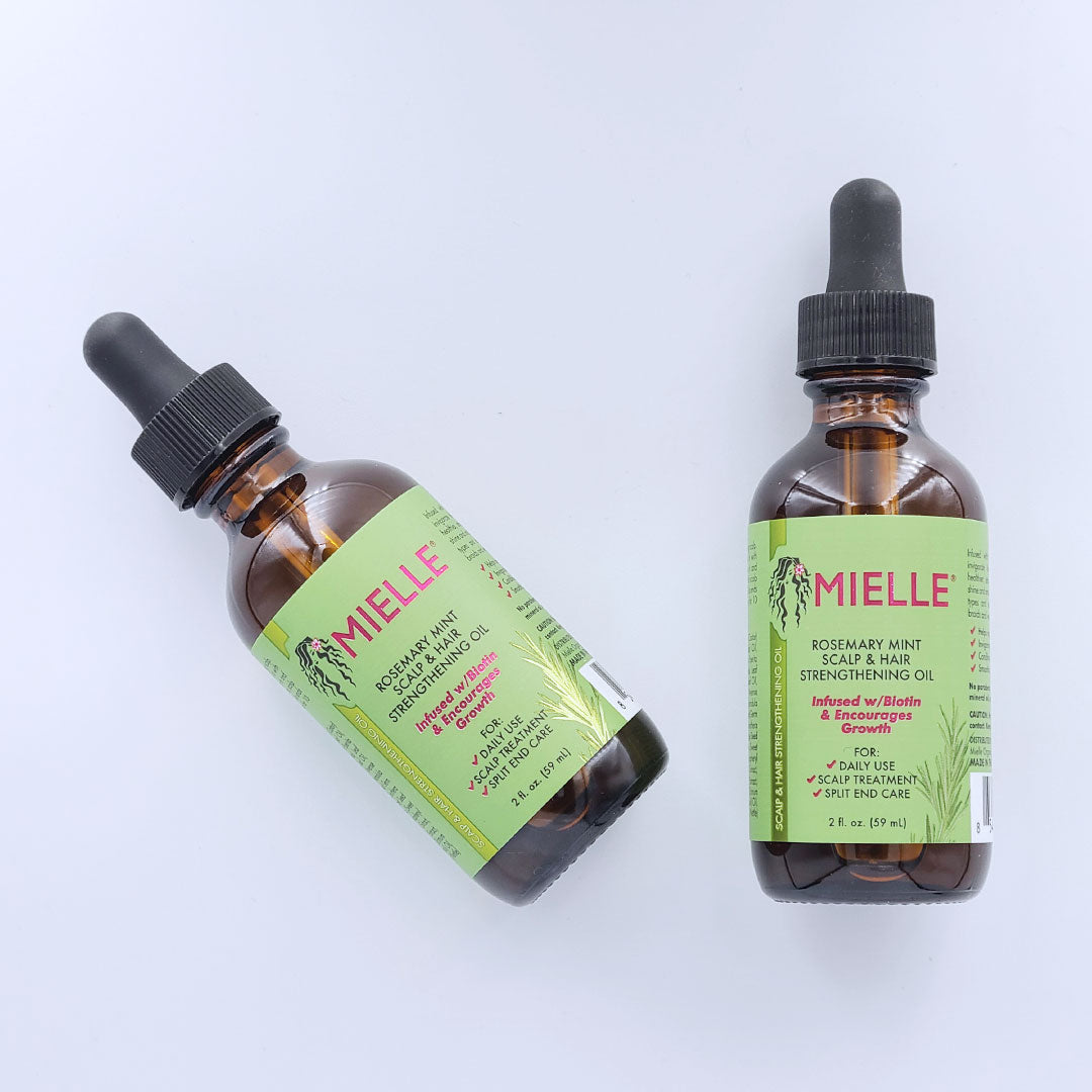 Two bottles of Mielle Rosemary Mint Scalp & Hair Strengthening Oil, one is straight and the other at a 45 degree angle, each is a 2 oz glass dropper bottle