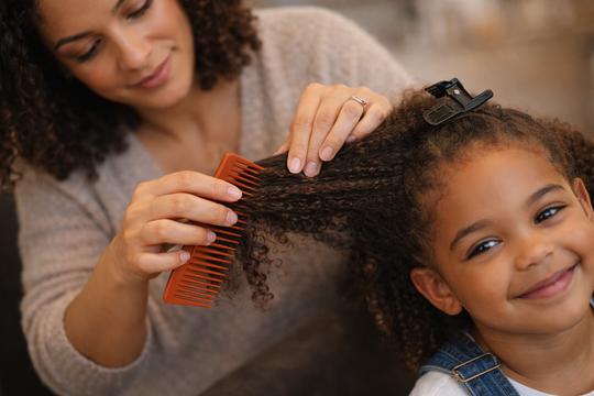 Parent gently detangling a child’s curly hair using proper sectioning technique during a training session.
